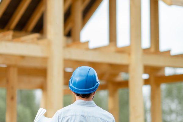 Builder with blueprints near the wooden house on the construction site